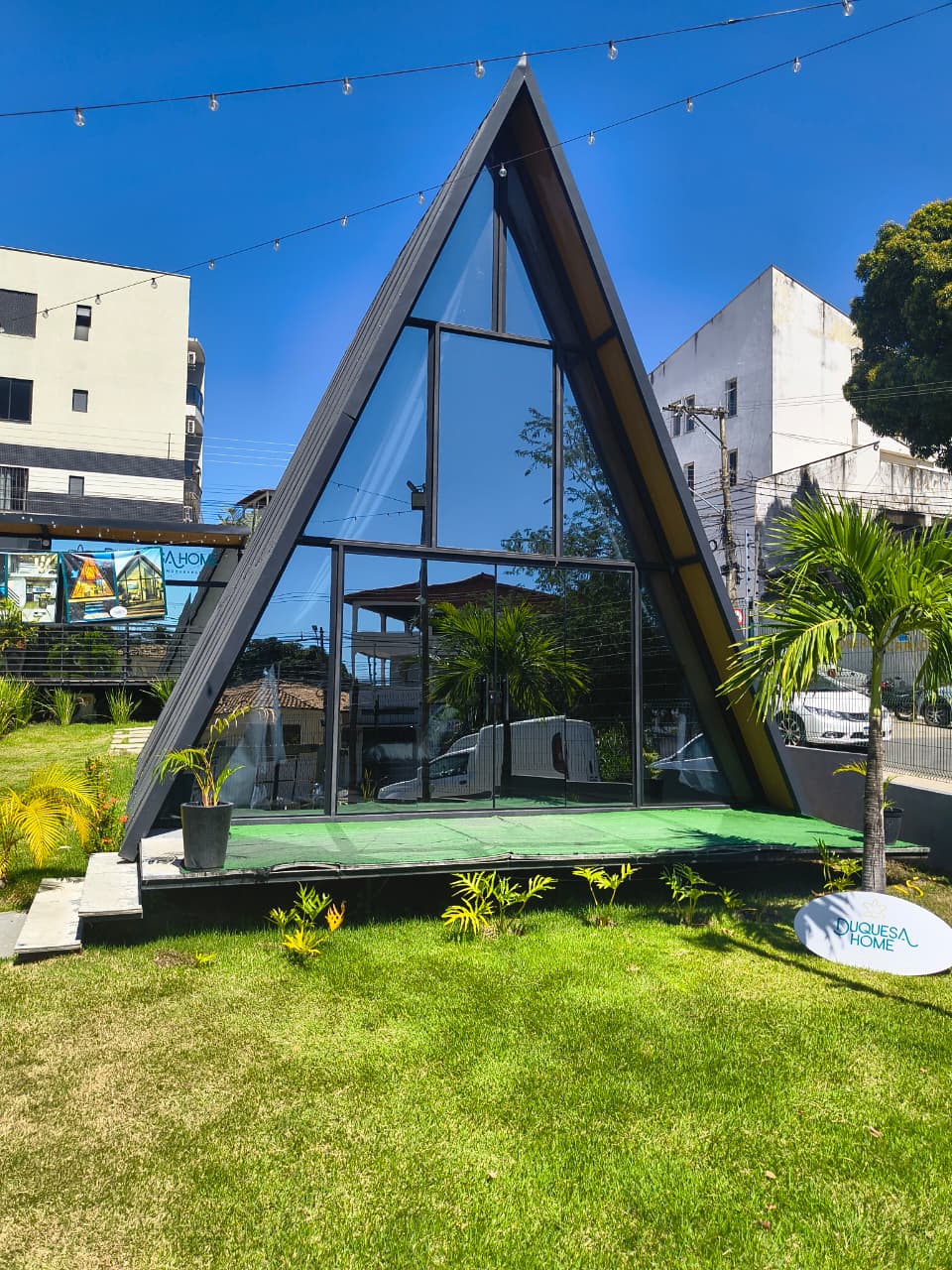 Fachada triangular de vidro do chalé Triângulo 60, com gramado e palmeira na frente