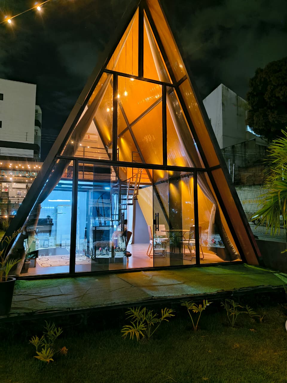 Chalé Triângulo com a fachada de vidro iluminada à noite