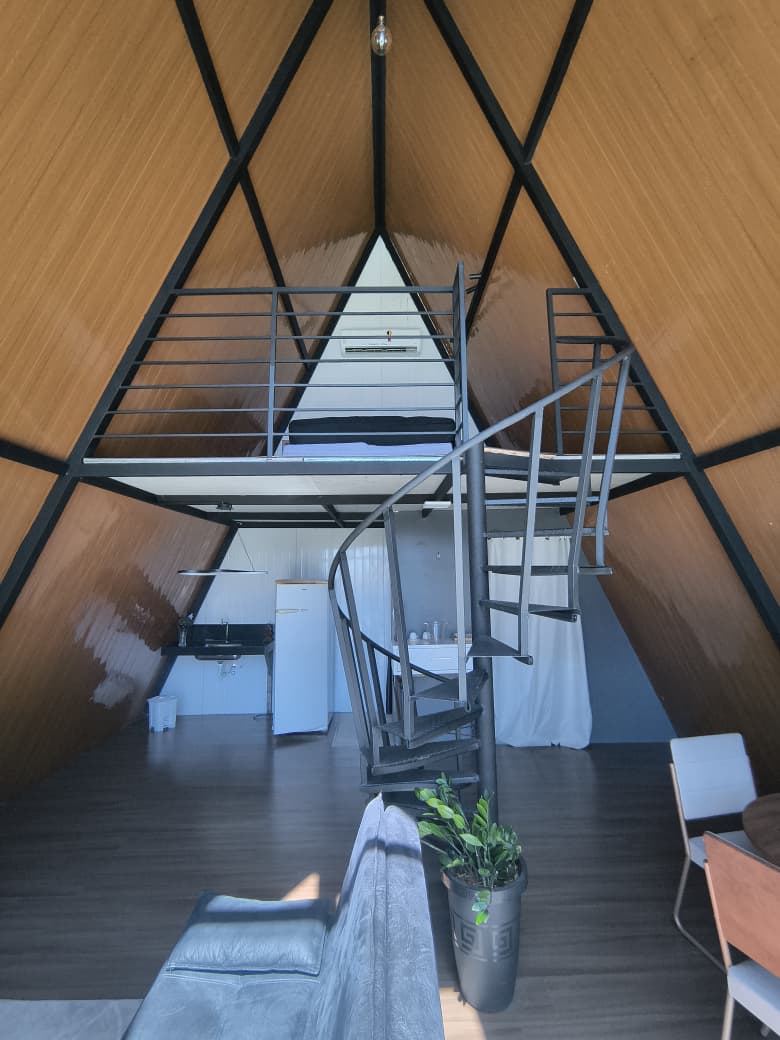 Sala com pé-direito alto, escada caracol e mezanino do chalé Triângulo 60
